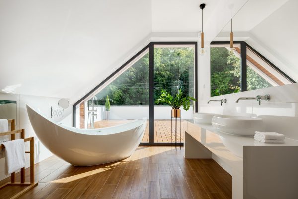 Elegant attic bathroom with stylish bathtub, wooden floor and balcony door